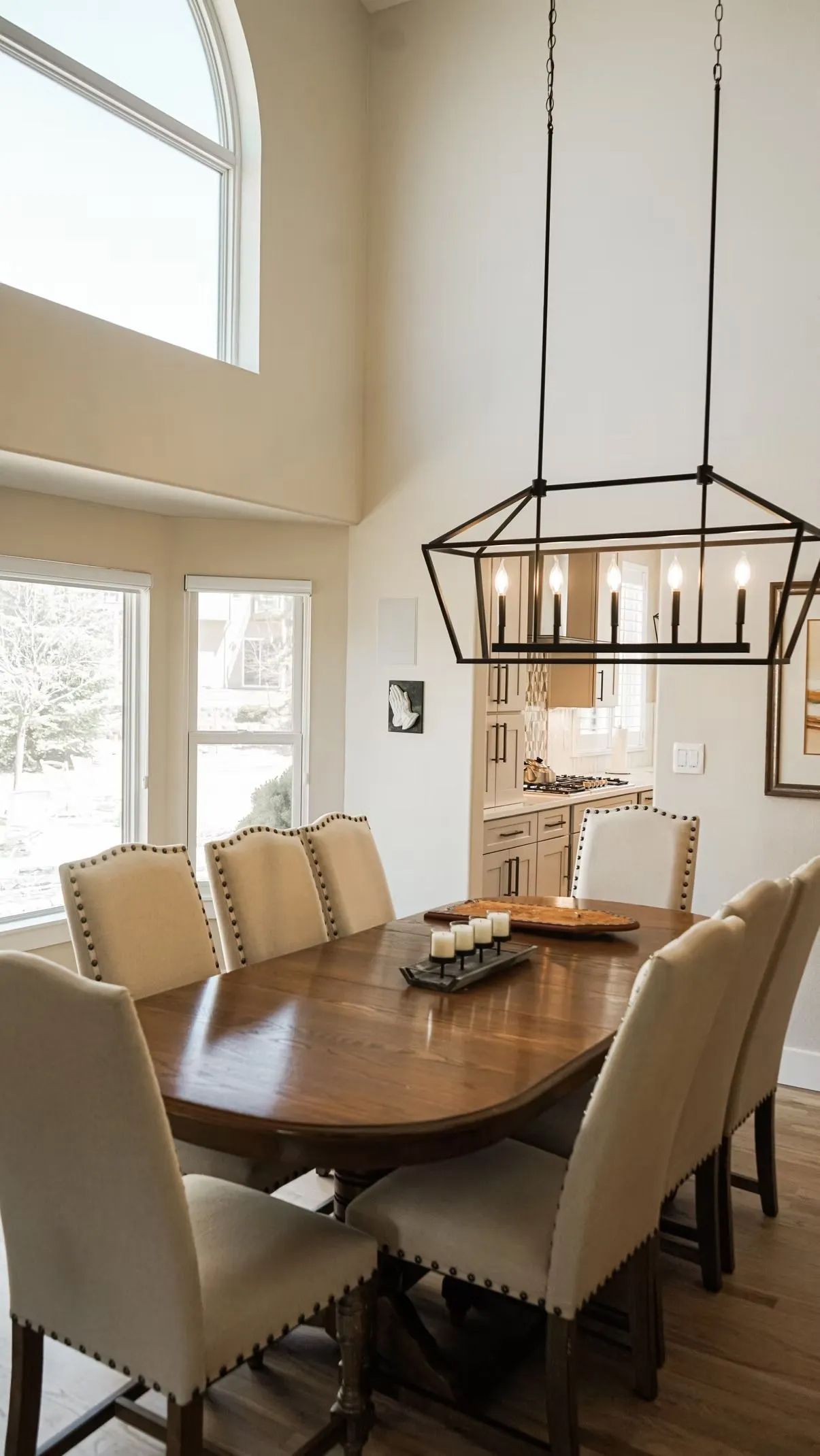 Elegant dining room with an oval wooden table, cream upholstered chairs, and a geometric chandelier. Large arched window.