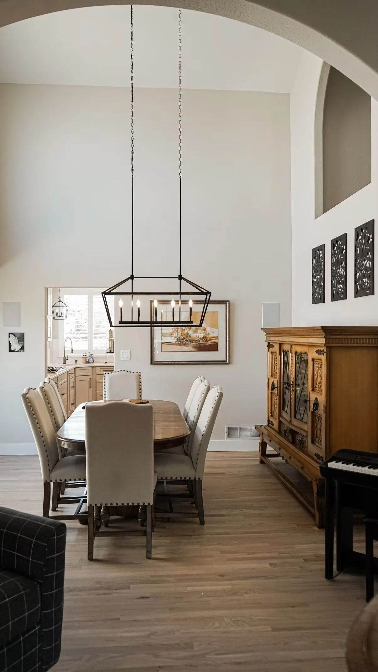 A bright dining room with a long table, chairs, and a wooden cabinet. High ceilings and archways create an open space.