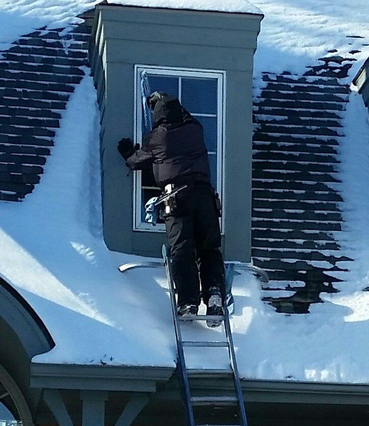 Person on a ladder cleaning a window on a snow-covered roof.