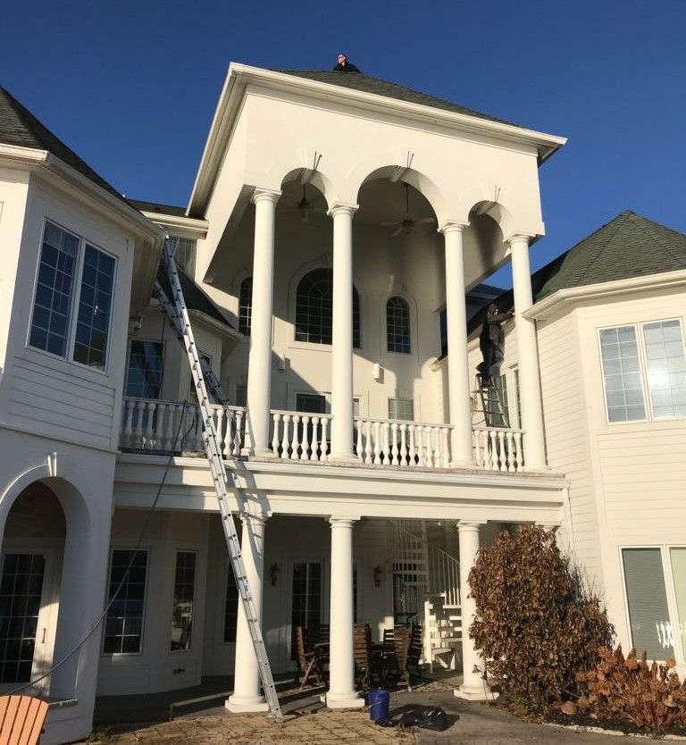 White house exterior with columns, multiple levels, and ladders. Person on a ladder working.