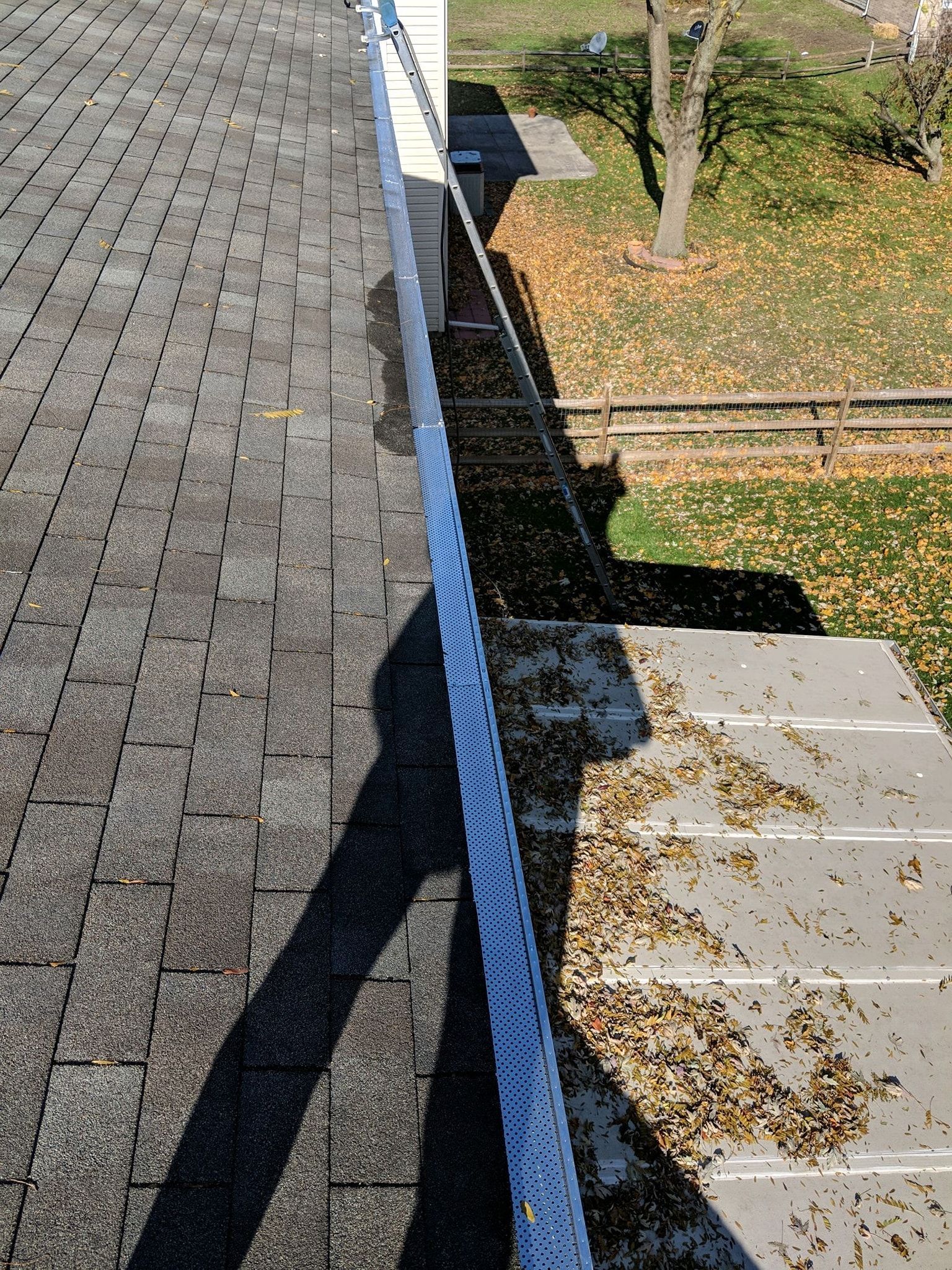 Rooftop view of gray shingles, white gutter filled with leaves, and a grassy yard.