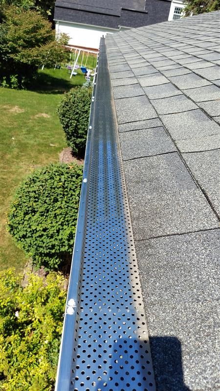 Gutter guard installed on a roof edge, covered in perforations, angled view.