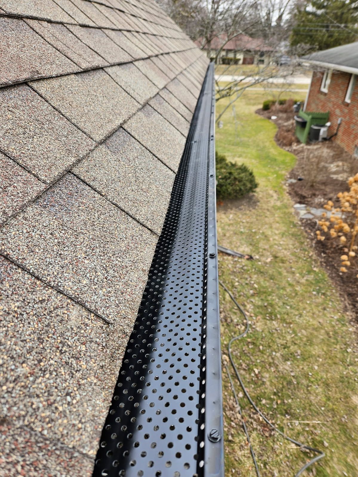 Black gutter guard on a roof, protecting against debris. Brown shingles, green grass, and a residential setting.