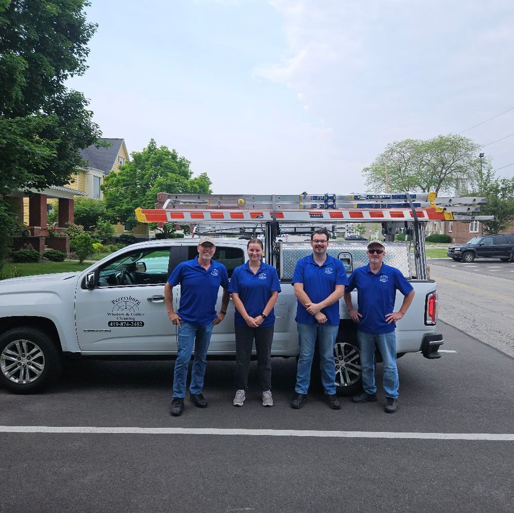 Four people in blue shirts stand beside a white truck with ladders. They are in front of houses on a street.