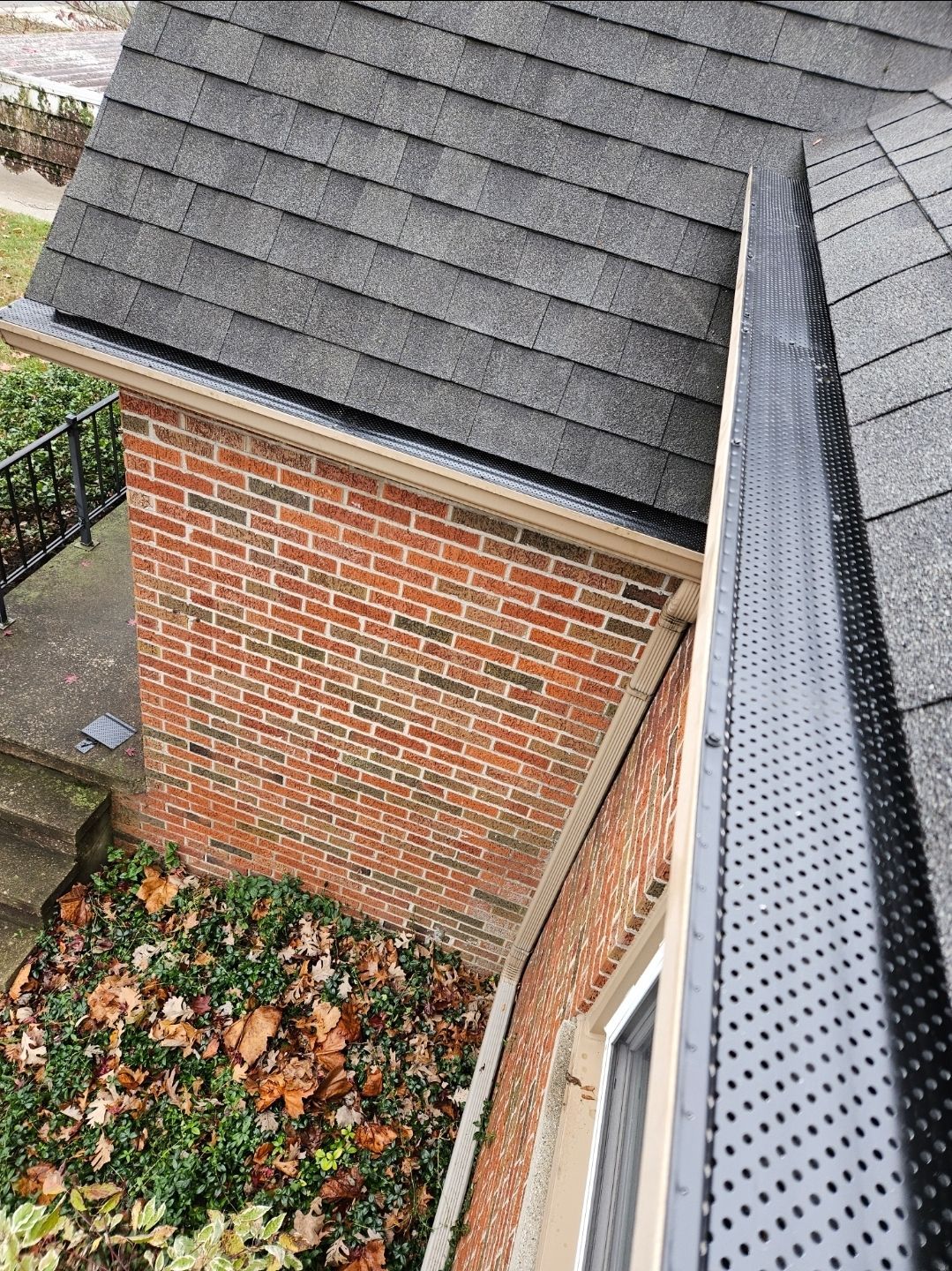 Gutters with mesh guards on a brick house with a shingled roof.