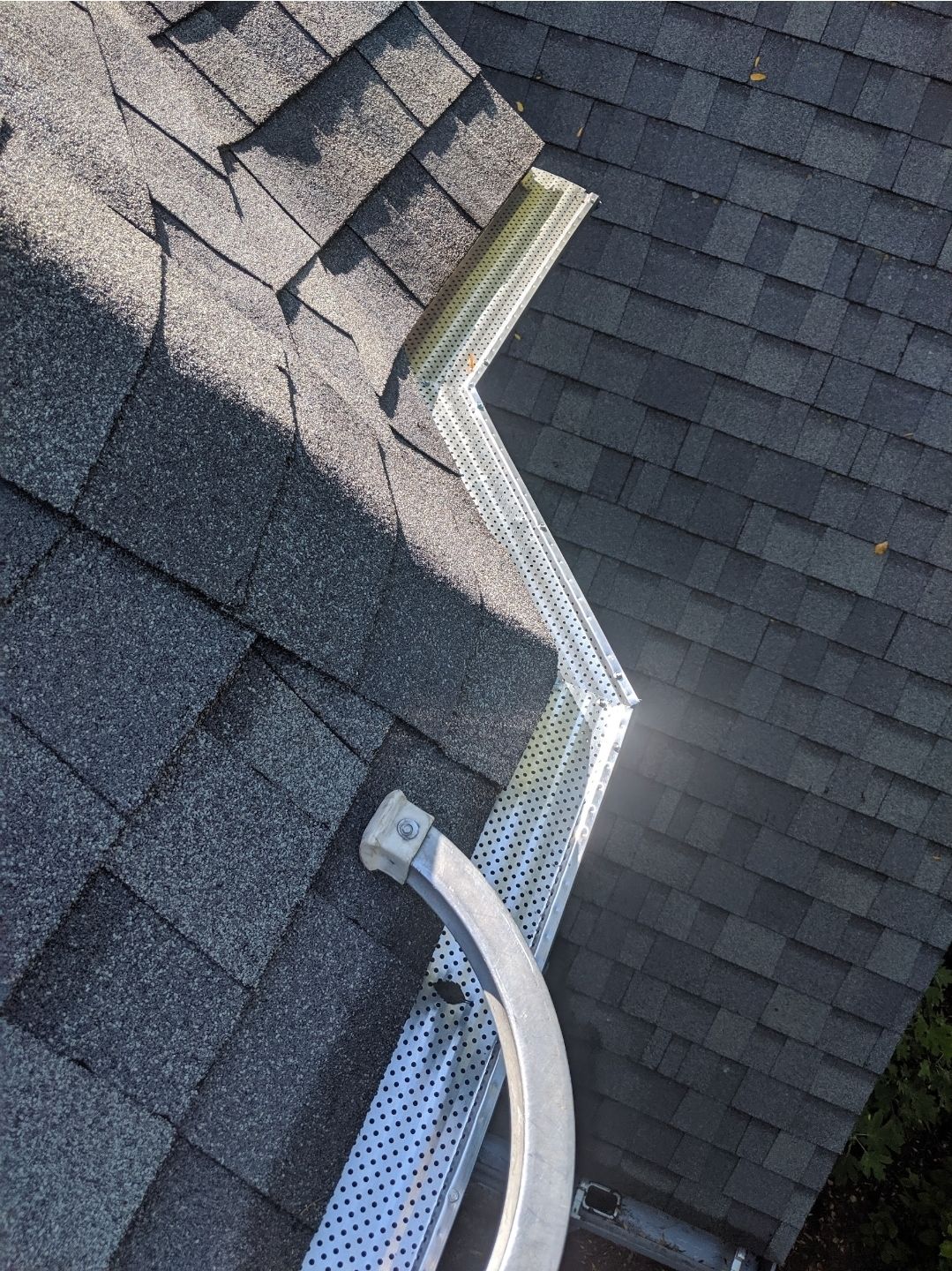 Overhead view of a gray asphalt shingle roof with a perforated white gutter.