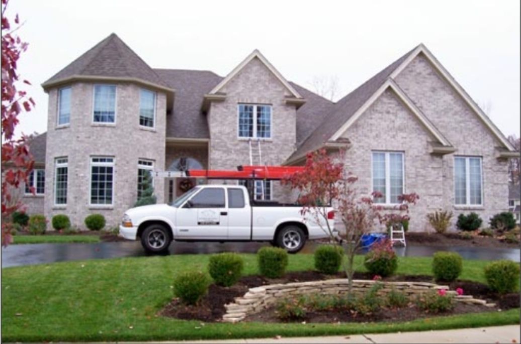 White truck parked in front of a brick house with a tower, green lawn, and landscaping.