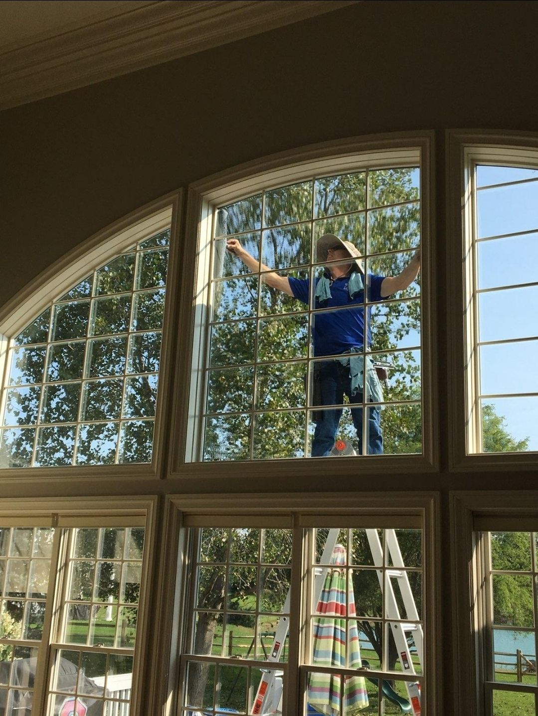Man cleaning large windows, wearing safety harness. Ladder visible.