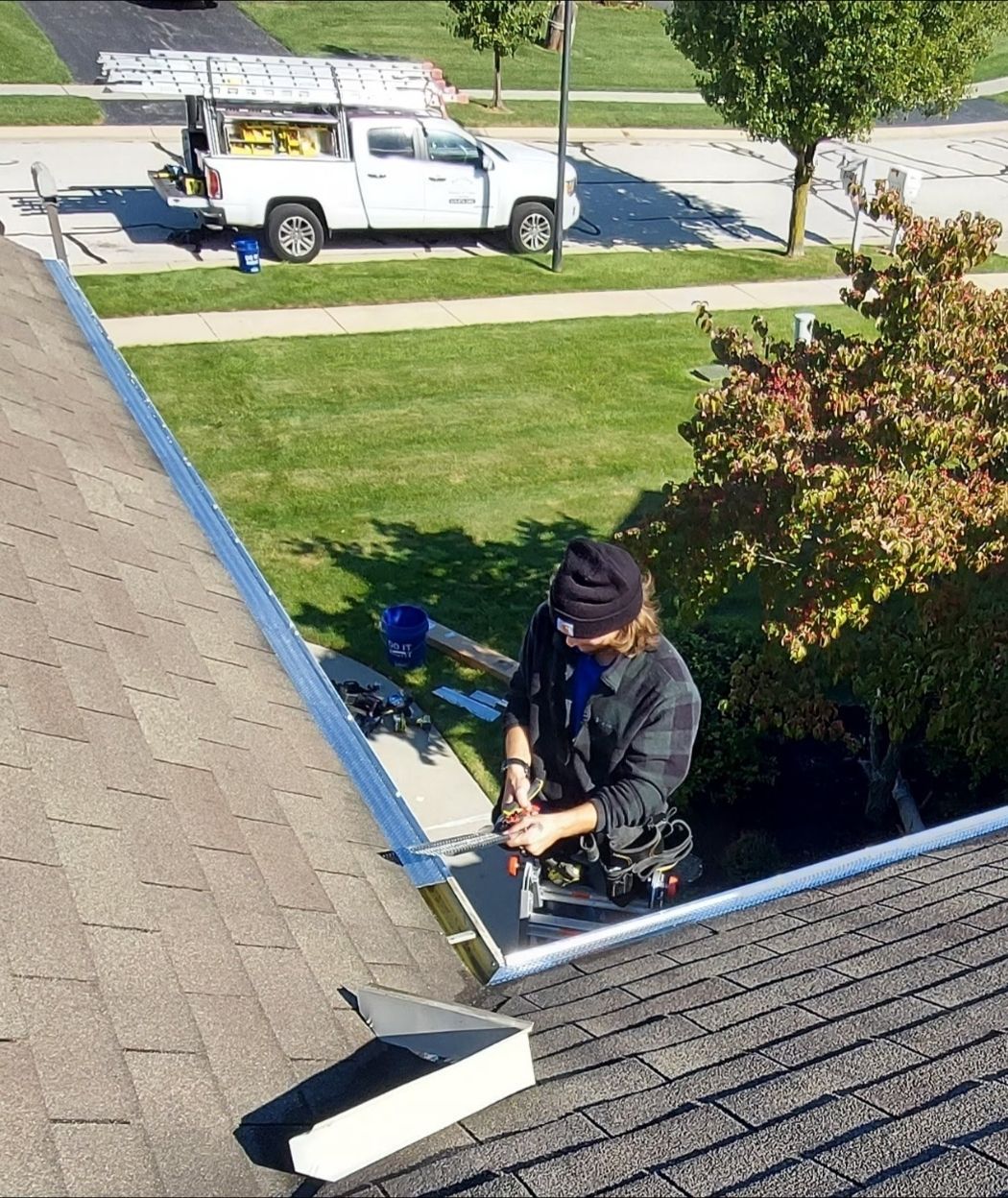 Person cleaning gutter on roof; white truck parked in background.