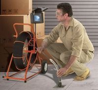 Man crouches beside an orange snowblower in a garage, inspecting the machine.