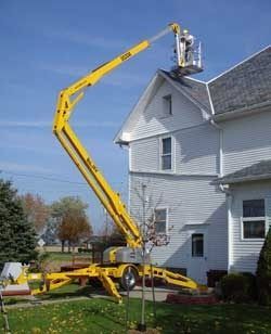 Boom lift extends to a worker on a roof beside a white house.
