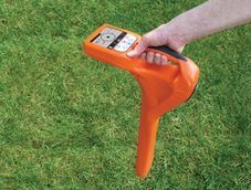 Hand holding an orange ground probe on green grass