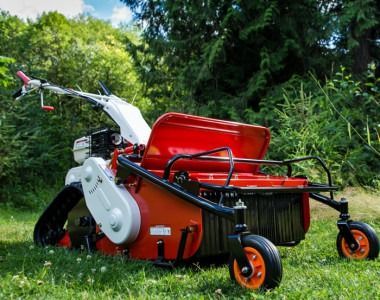 Red lawn mower on grass in a garden, with orange wheels and a red grass catcher tank