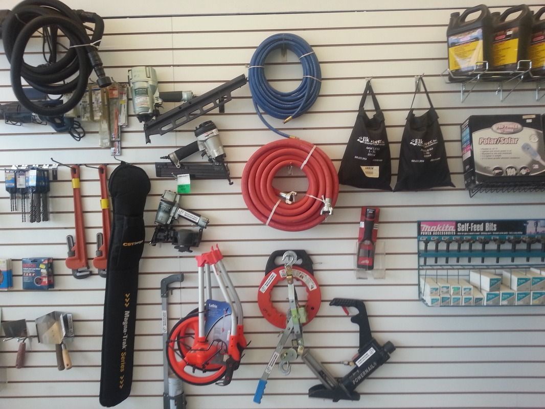 Assorted tools and accessories displayed on a slatwall in a shop, including hoses, belts, and bags.