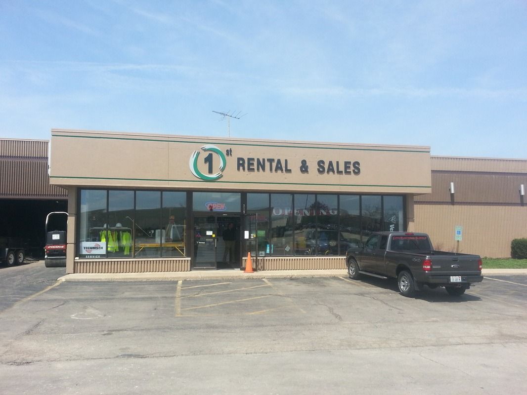 Storefront with sign reading “Rental & Sales,” glass windows, and a black pickup truck parked outside.