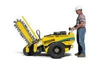 Worker standing beside a yellow asphalt-cutting machine with a raised blade.