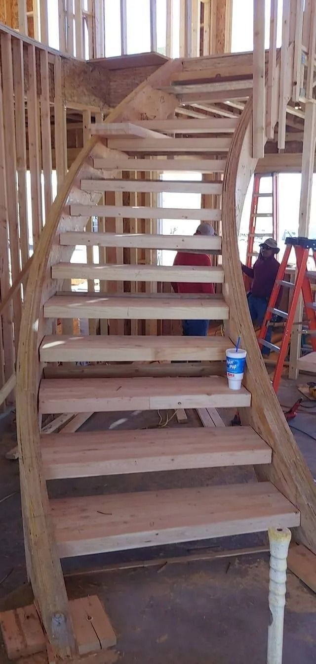 Wooden staircase under construction. A worker is seen near a ladder.