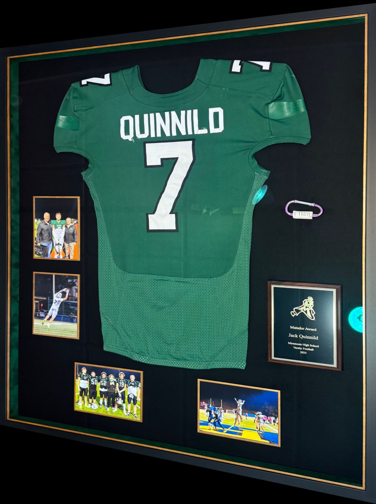 Framed football jersey of Quinnild with the number 7, displayed with photos and a plaque. Jersey is green with white lettering on black background.