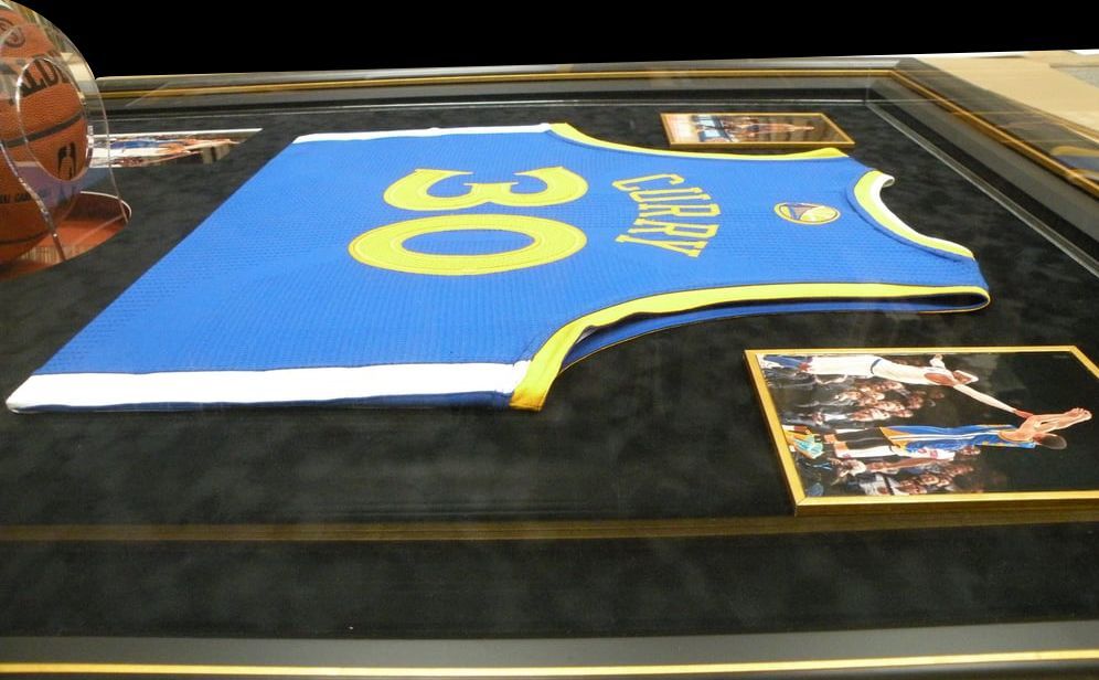 Framed Golden State Warriors jersey with the number 30, alongside photos. Blue and yellow colors on a black background, in a custom frame.