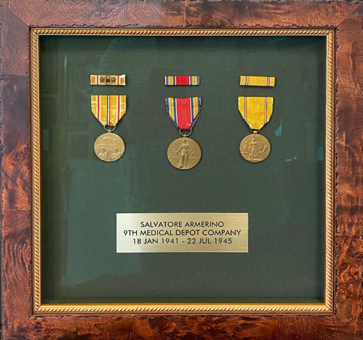 Framed military medals with a nameplate on green background. The frame is brown with a gold inner border.