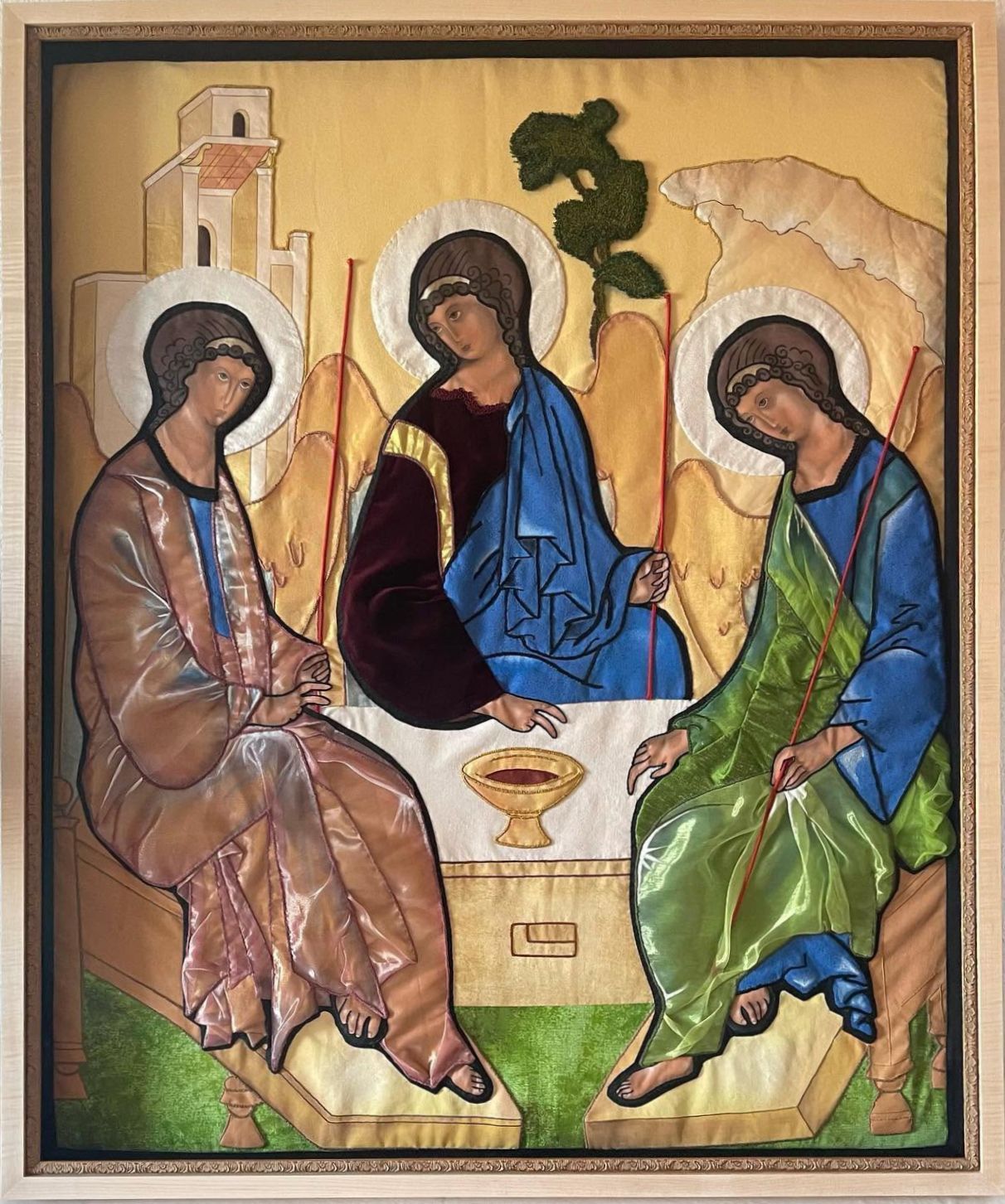 Three haloed figures seated around a small table in a religious icon, with gold background and deep blue robes