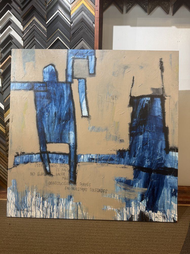 Abstract painting with a blue figure and tower on a tan background, some text at the bottom, in front of frame samples.