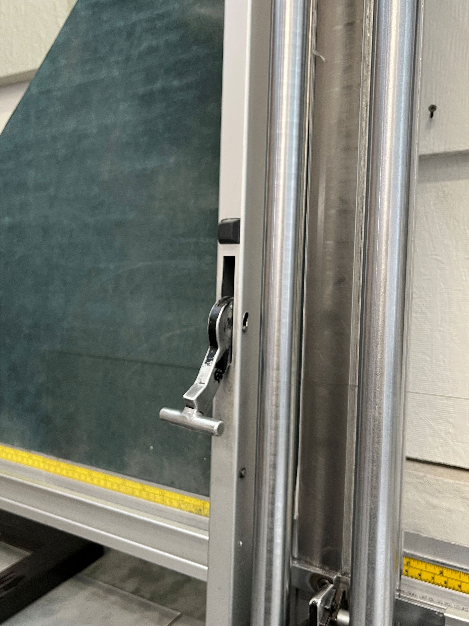 Glass cutting machine with lever and metal guide rails. Green glass panel visible.