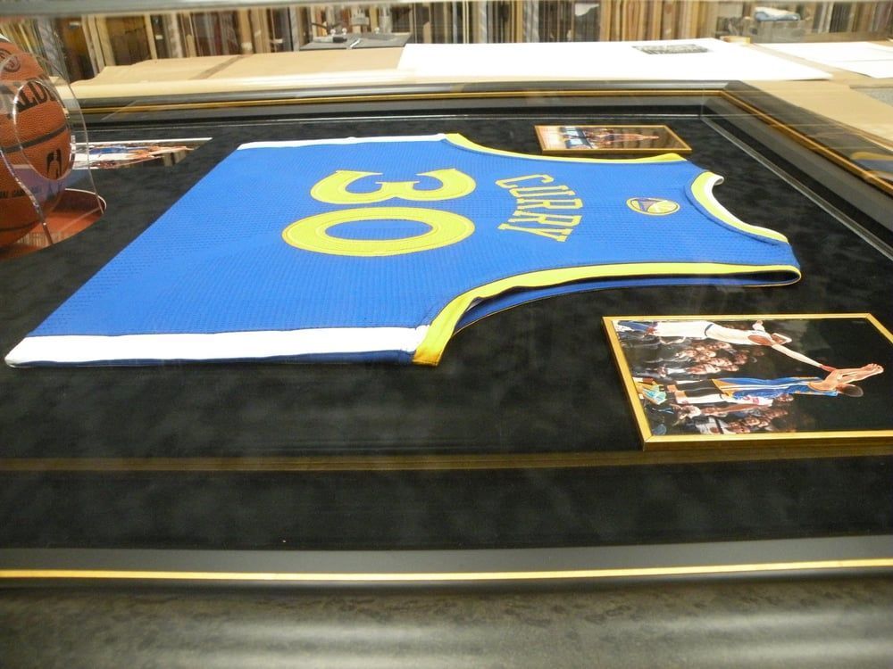 Framed Golden State Warriors jersey with the number 30, alongside photos. Blue and yellow colors on a black background, in a custom frame.