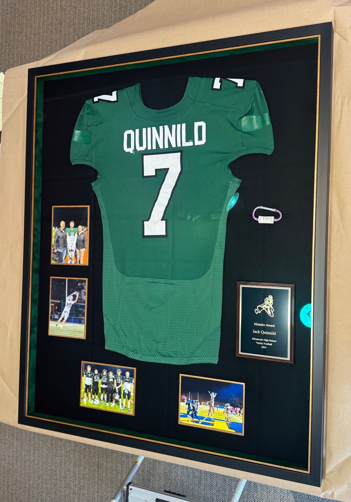 Framed football jersey of Quinnild with the number 7, displayed with photos and a plaque. Jersey is green with white lettering on black background.