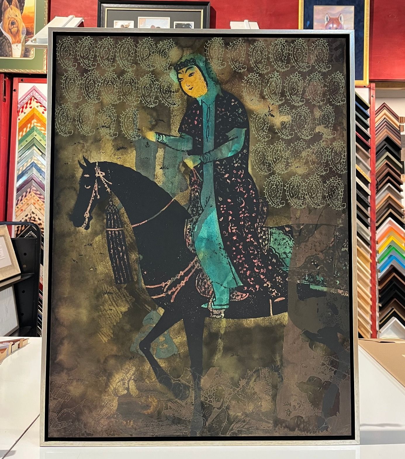 woman in a teal cloak on a black horse against a gold and brown background, framed