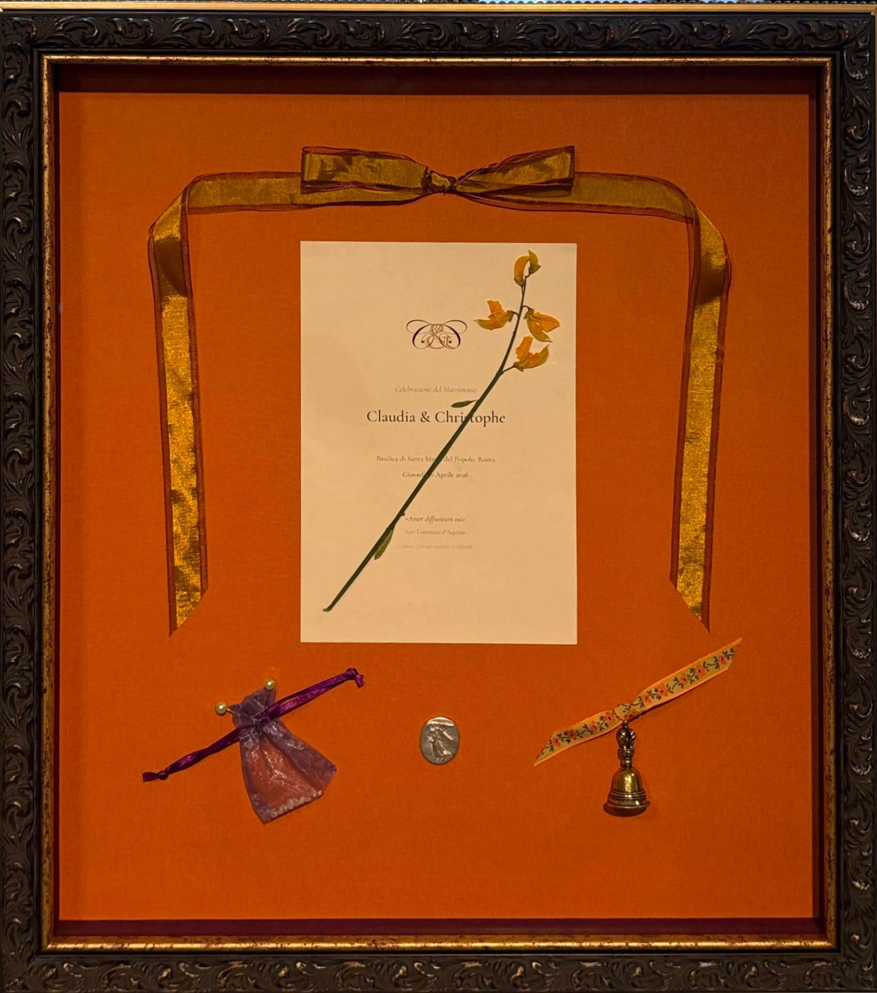 Framed orange wall art with ribbon, central drawing, and two decorative objects at the bottom