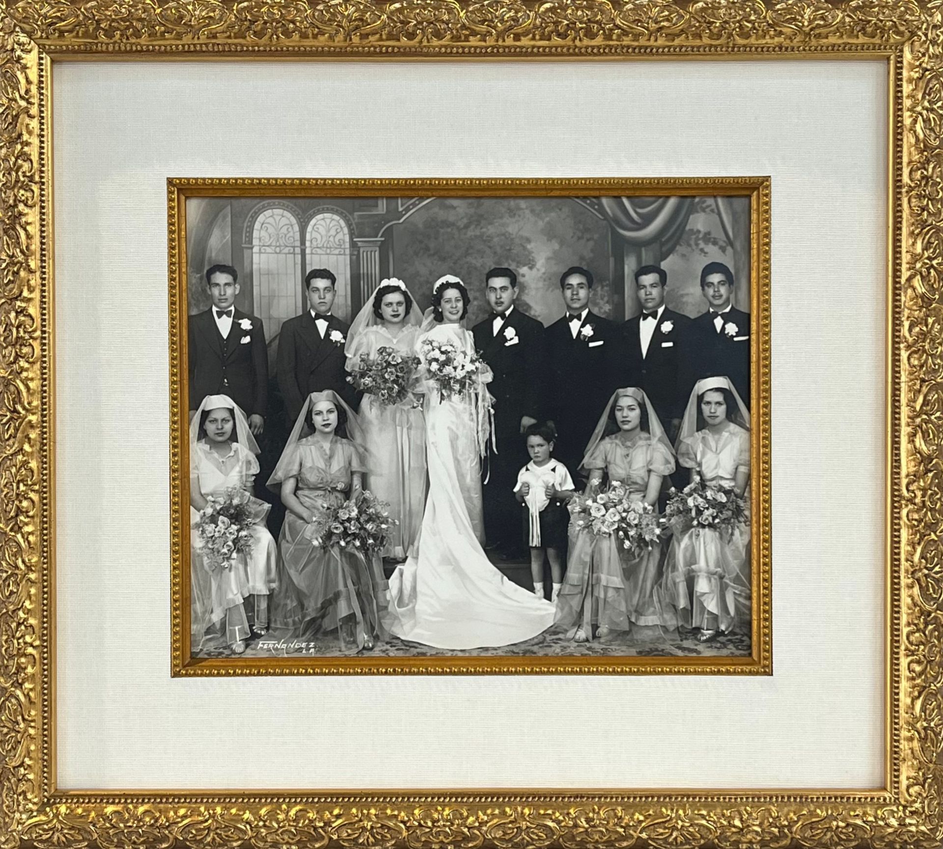 Framed black-and-white wedding portrait with bride, groom, attendants, and family in formal attire