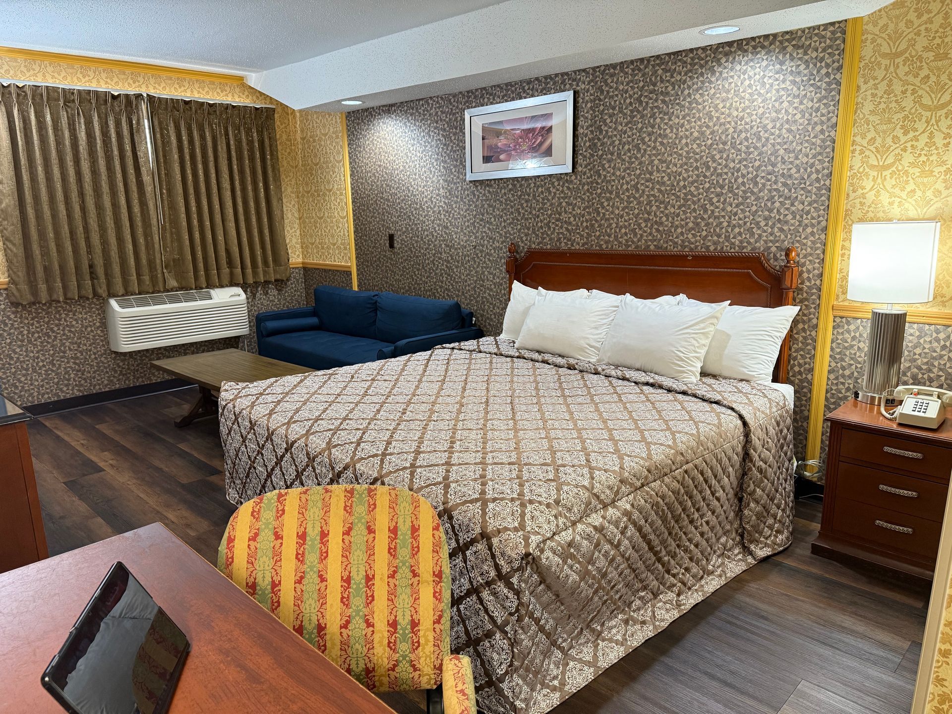 Hotel room with a bed, couch, desk, and nightstand. Brown and gold color scheme.