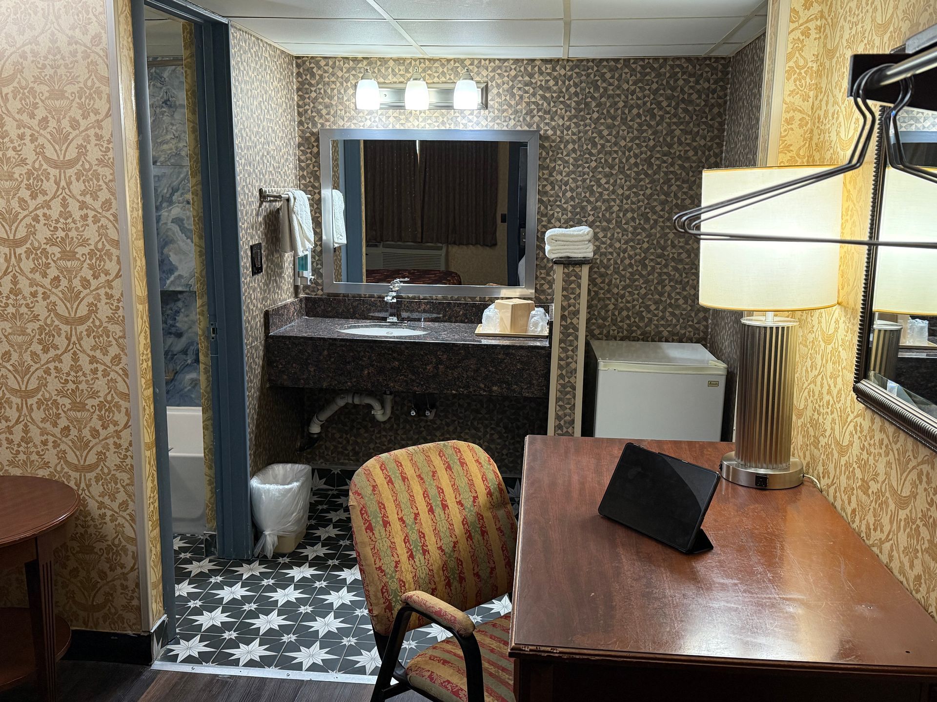 Hotel room interior with desk, bathroom, and patterned wallpaper.