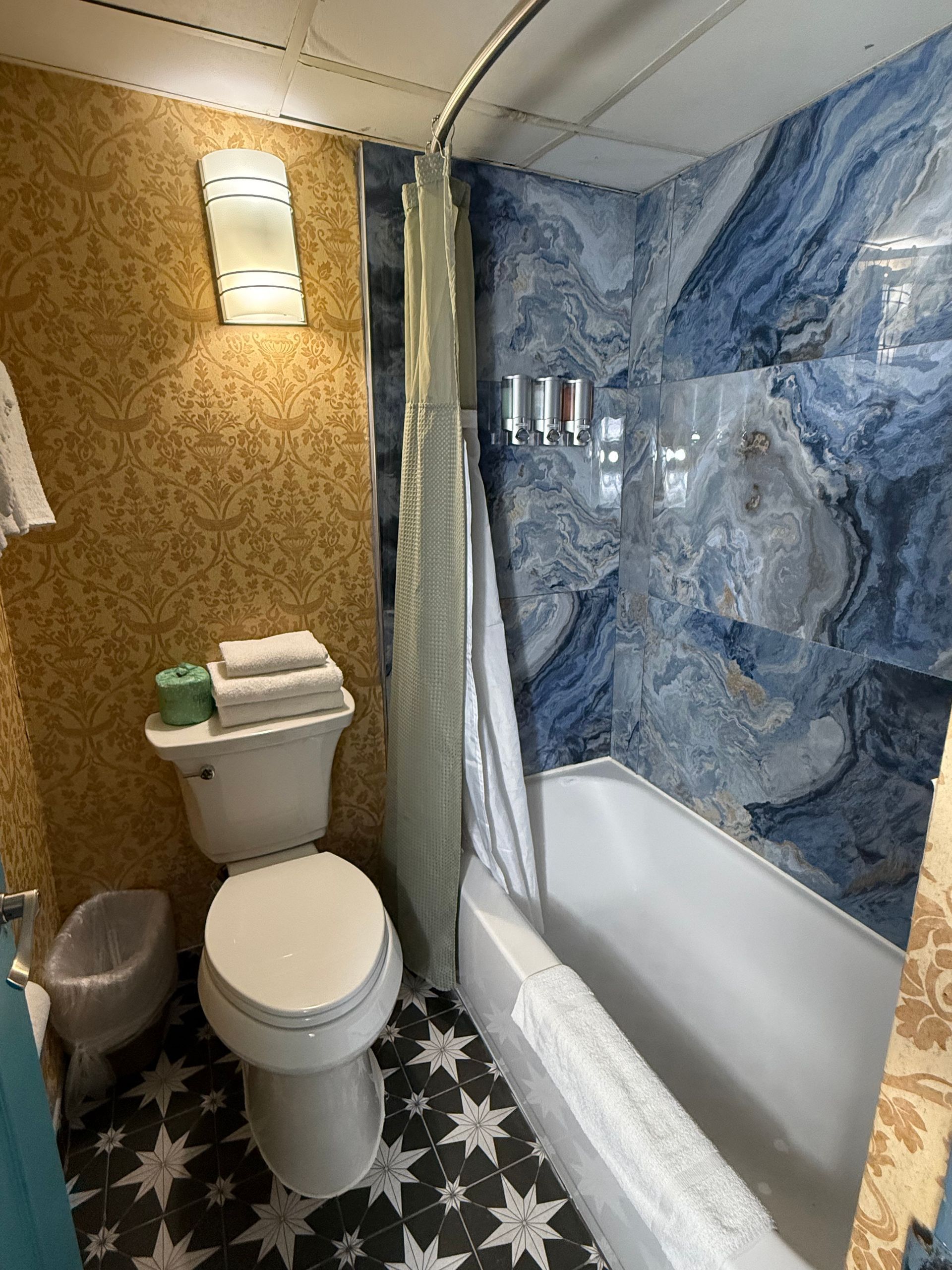 Bathroom with patterned wallpaper, blue marble shower surround, and star-patterned floor.