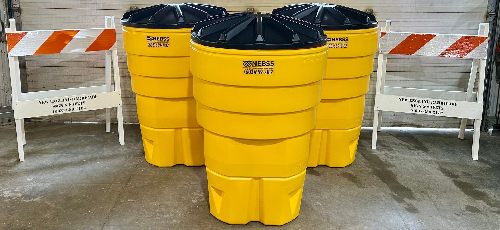 Three yellow trash cans with black lids are sitting next to each other.
