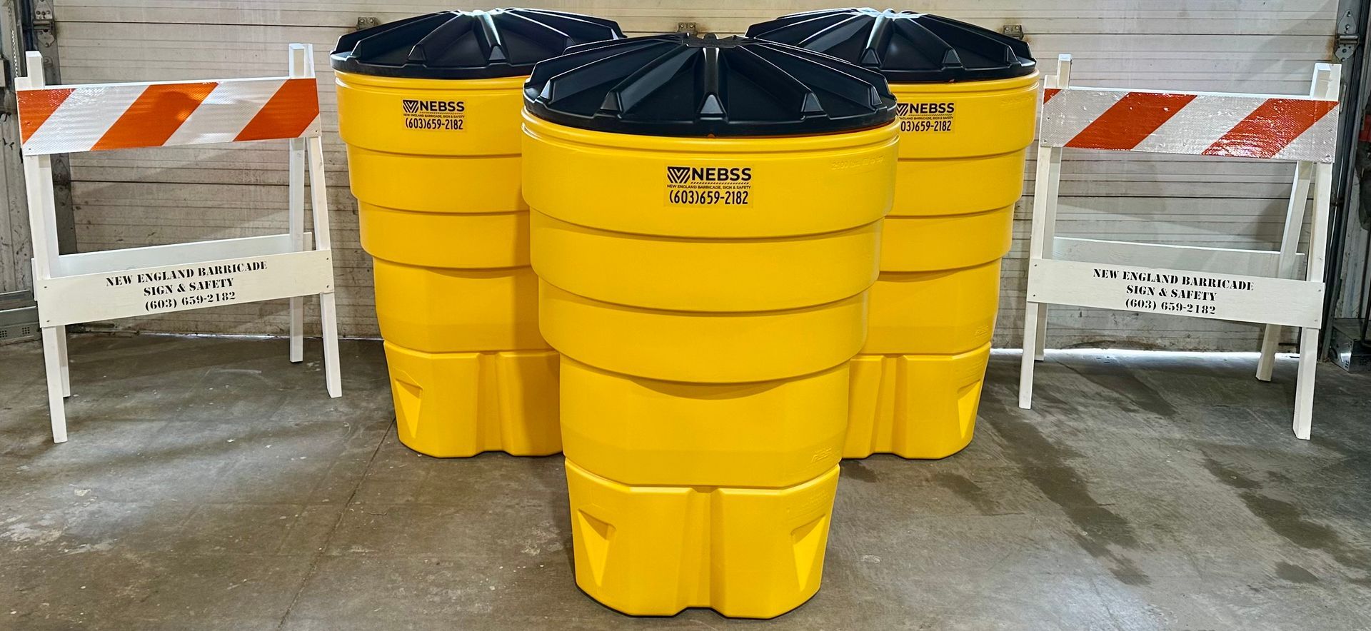 Three yellow trash cans with black lids are sitting next to each other.