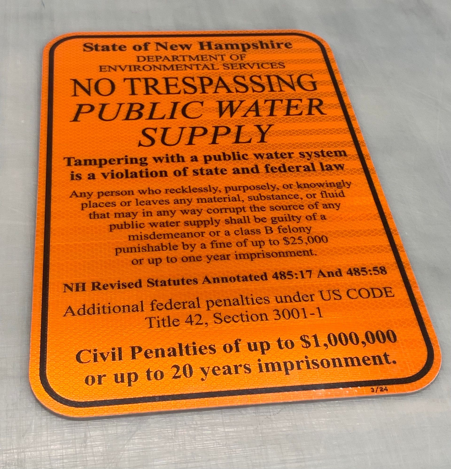 An orange sign that says no trespassing public water supply