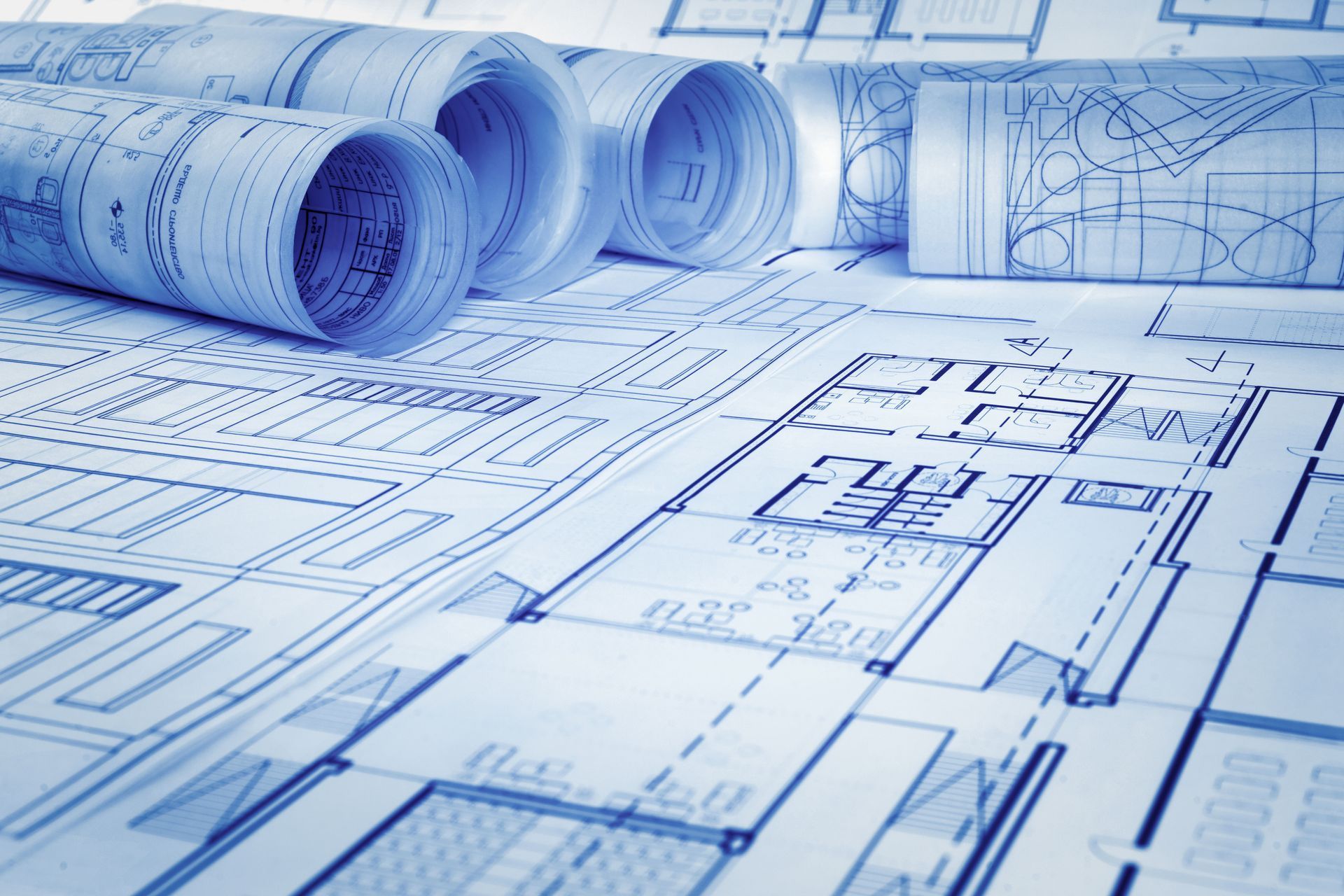 Blue architectural blueprints and rolled plans laid out on a drafting surface