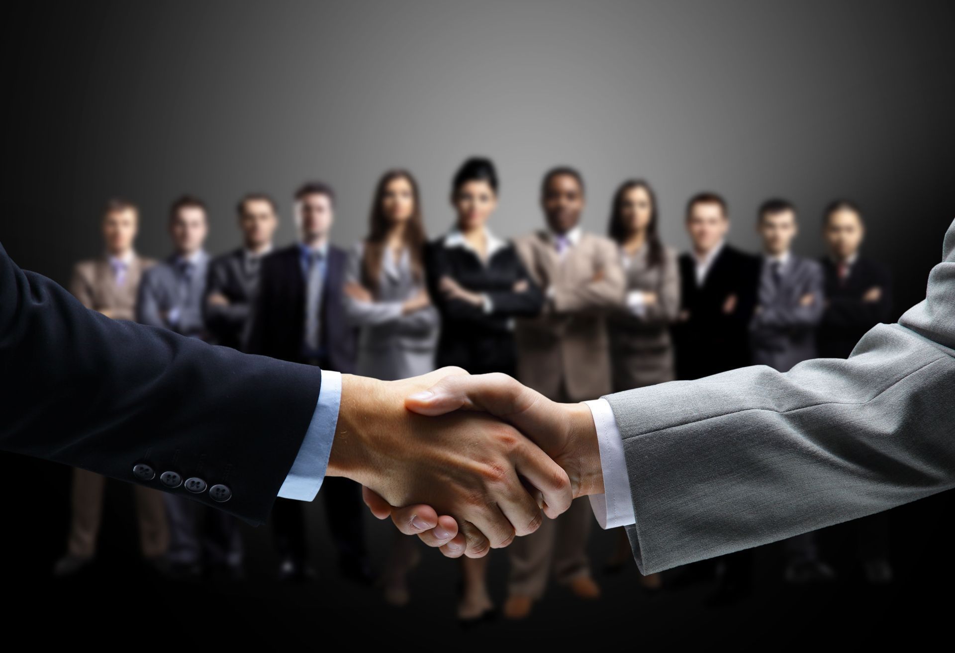 Businesspeople shaking hands in front of a blurred team, symbolizing a deal or partnership
