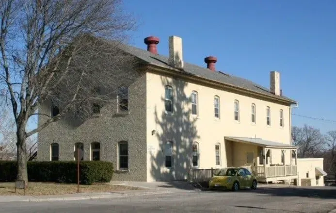 Cream-colored house with chimneys, bare trees, and a yellow car parked by the driveway.