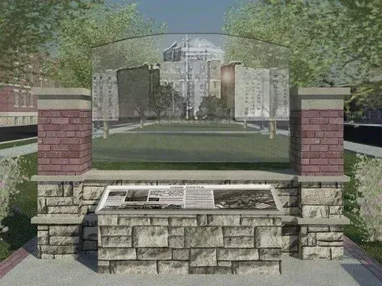 Stone memorial wall and engraved plaque in a park, with a campus building in the background.