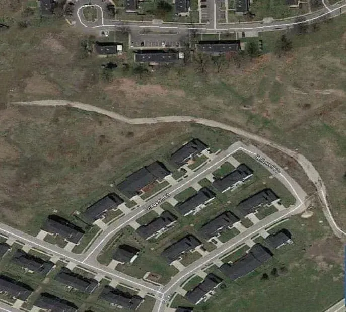 Aerial view of a small residential housing complex with dark roofs, roads, and surrounding grass.