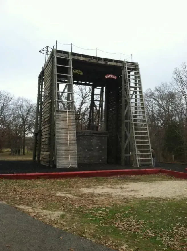 Outdoor wooden stage structure with ladders on both sides in a park, surrounded by bare trees.