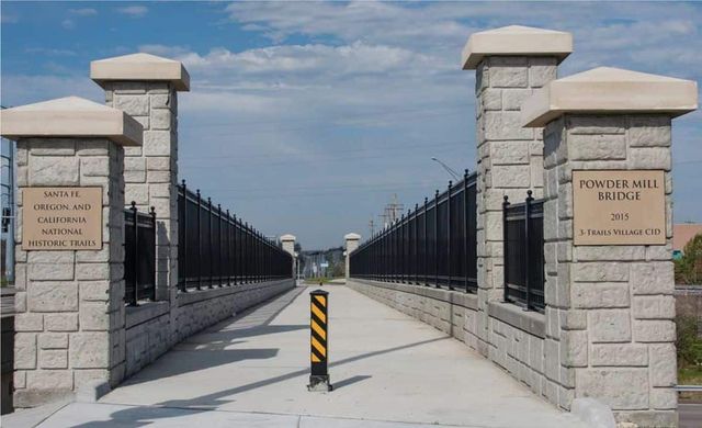 Stone entrance gate with black fencing and a narrow road leading inward under a cloudy sky