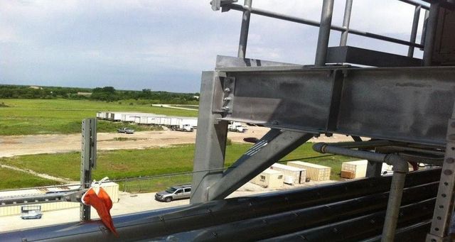 Construction platform overlooking a grassy site, with an orange-clad worker near metal beams and scaffolding.