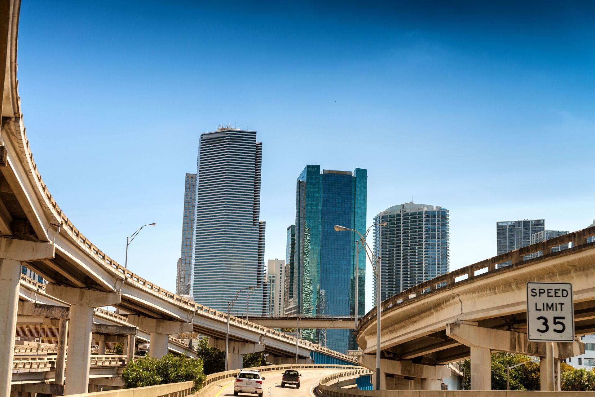 City freeway interchange framing downtown skyscrapers under a clear blue sky.