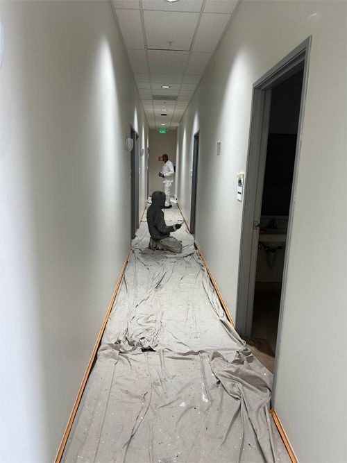 A man is kneeling down in a long hallway covered in a tarp.