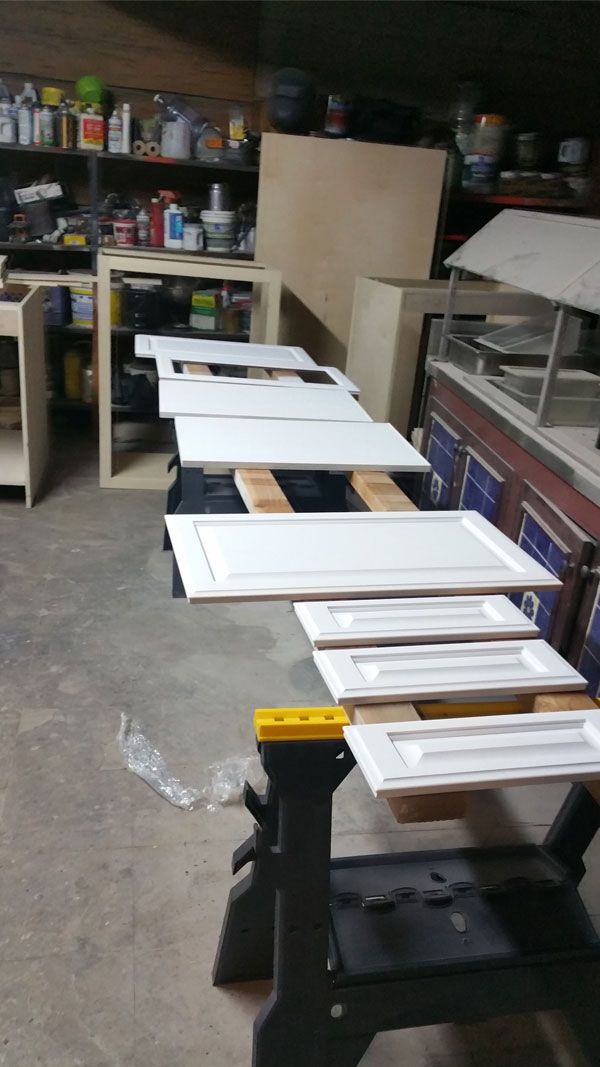 A row of white cabinet doors are sitting on a workbench.
