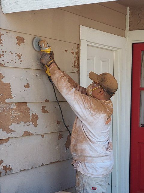 A man wearing a mask is sanding a wall.